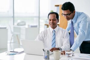 Two men in a room looking at a laptop.